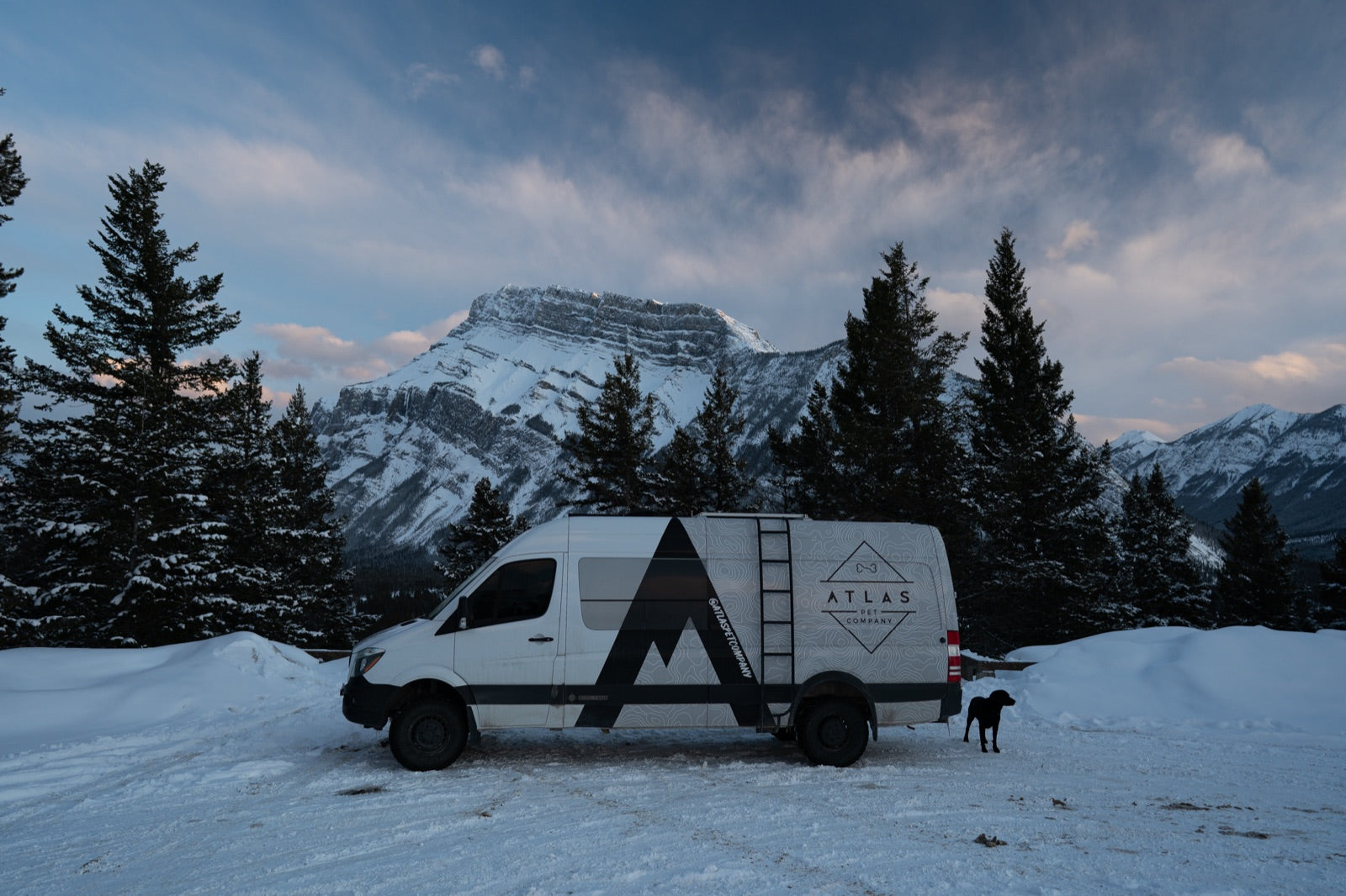 Atlas Pet Company Sprinter van parked in deep mountain snow with a dog, van life adventure scene