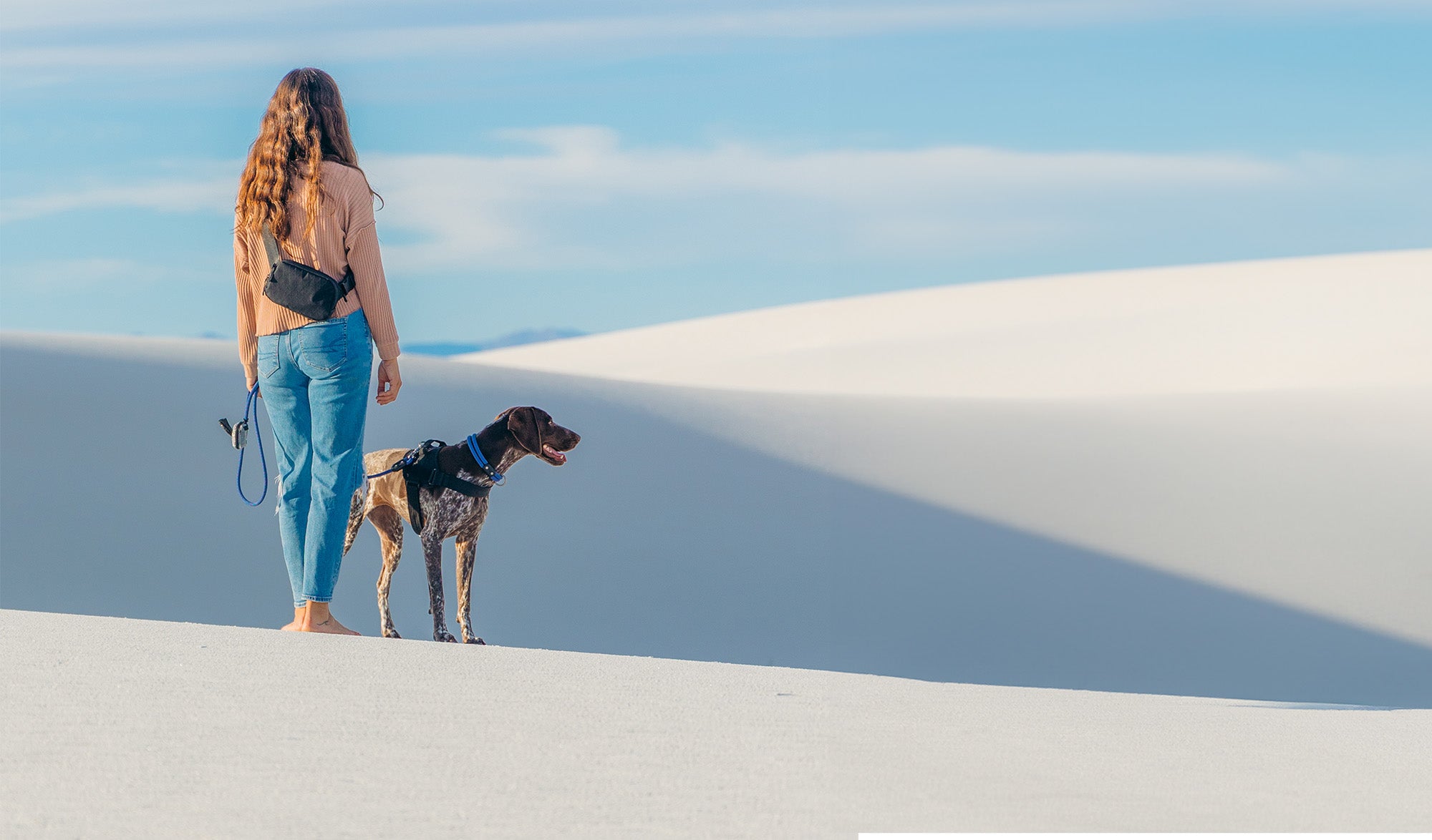 woman wearing the atlas pet company lifeitme belt bag while standing in white sand desert with a dog